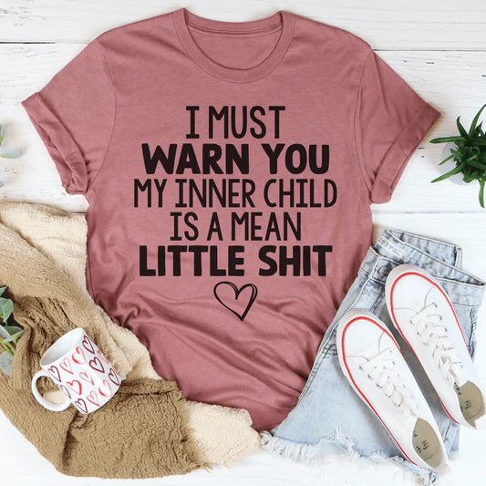 Pink t-shirt with humorous text, placed on a surface with casual items like jeans and shoes.