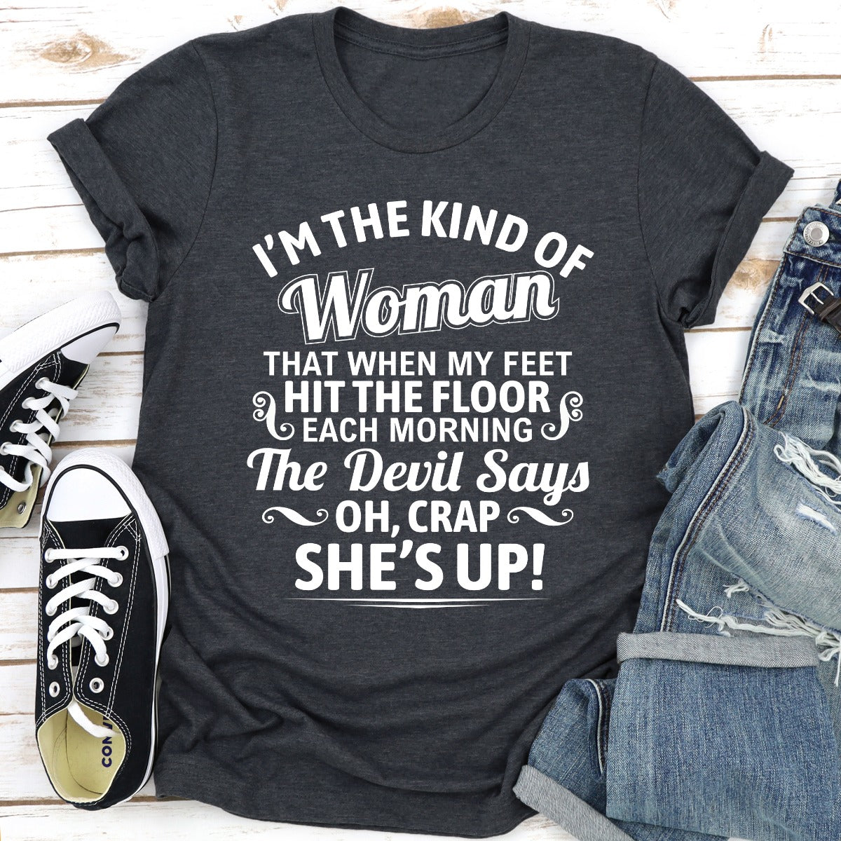 Dark gray t-shirt with humorous text design on a wooden surface with shoes and jeans.