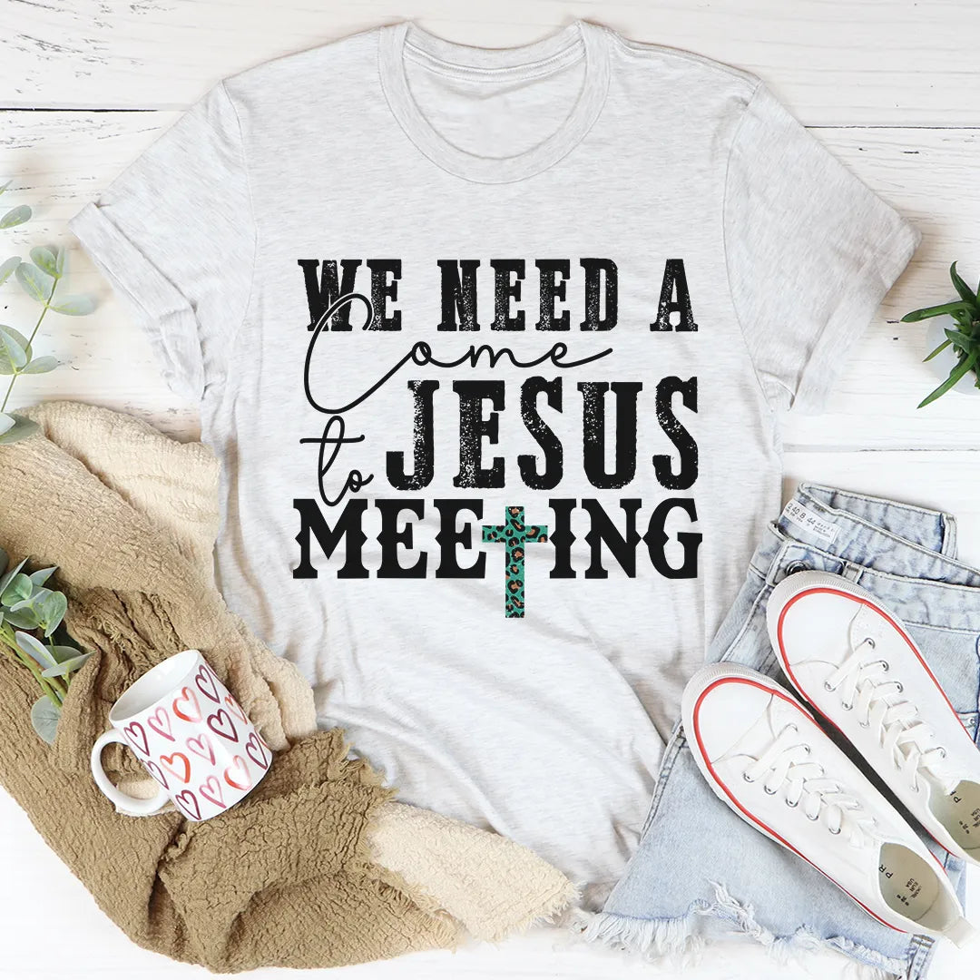 White t-shirt with 'We need a Jesus meeting' text on a white background with casual items around.