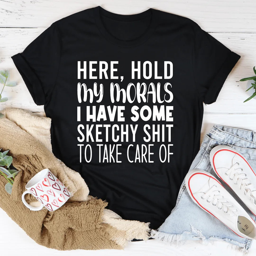 Black t-shirt with humorous text on a casual setting with shoes, mug, and blanket.
