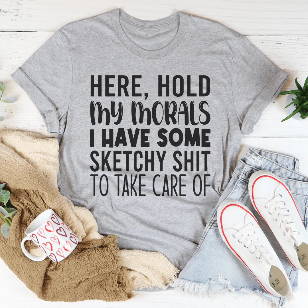 Gray t-shirt with humorous text, placed on a surface with shoes and a mug.