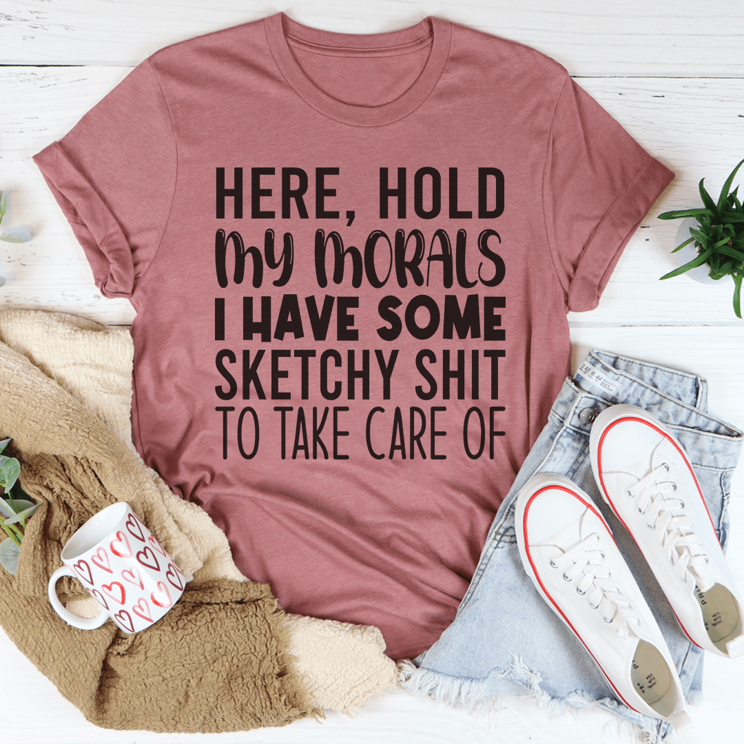 Mauve t-shirt with humorous text, placed on a white surface with casual items like jeans and sneakers.
