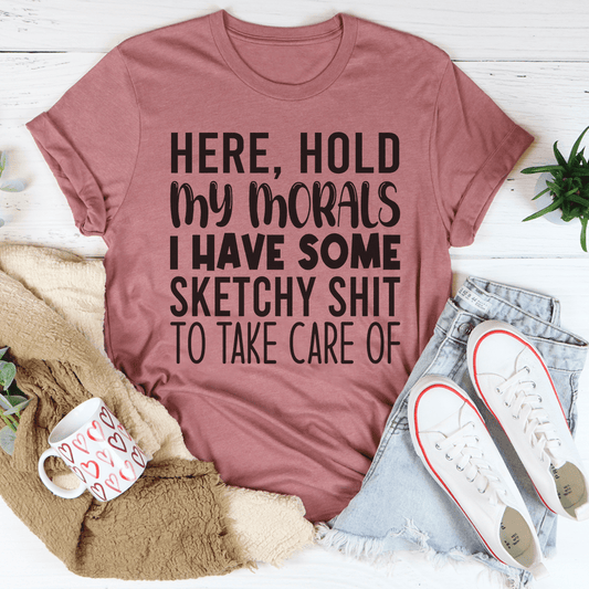 Mauve t-shirt with humorous text, placed on a white surface with casual items like jeans and sneakers.