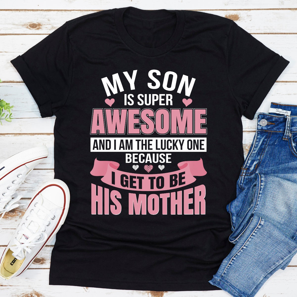 Black t-shirt with text 'My son is super awesome and I am the lucky one because I get to be his mother' on a wooden surface with jeans and sneakers.
