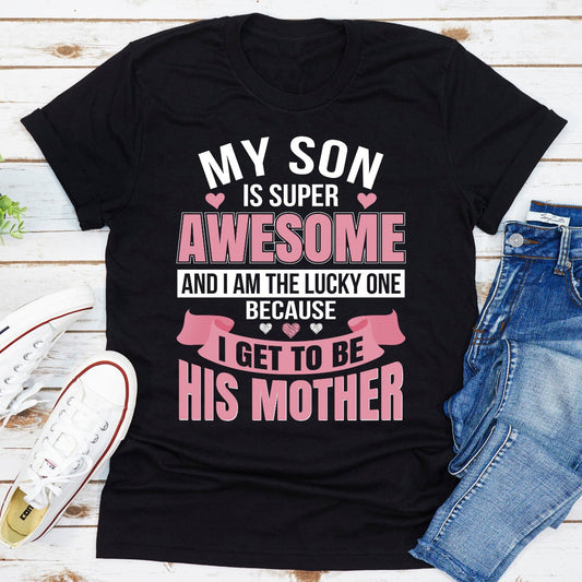 Black t-shirt with text 'My son is super awesome and I am the lucky one because I get to be his mother' on a wooden surface with jeans and sneakers.