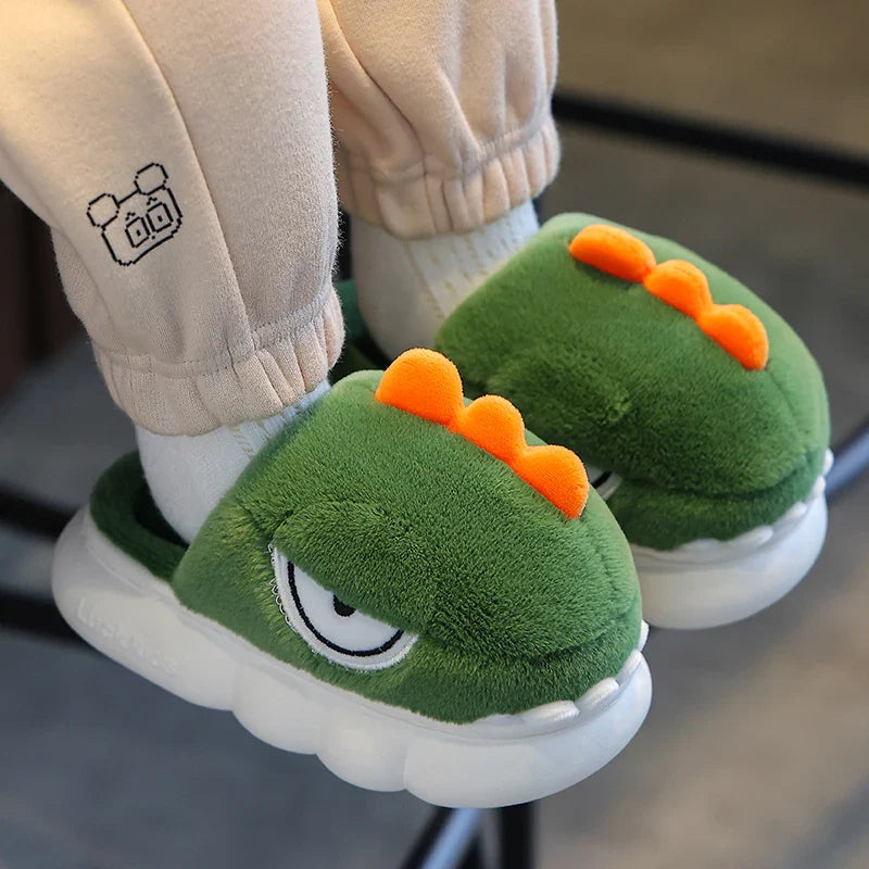 Green dinosaur-themed slippers worn with beige pants on a blurred background