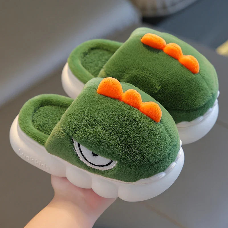 Green children's slippers with dinosaur design held by a hand on a neutral background