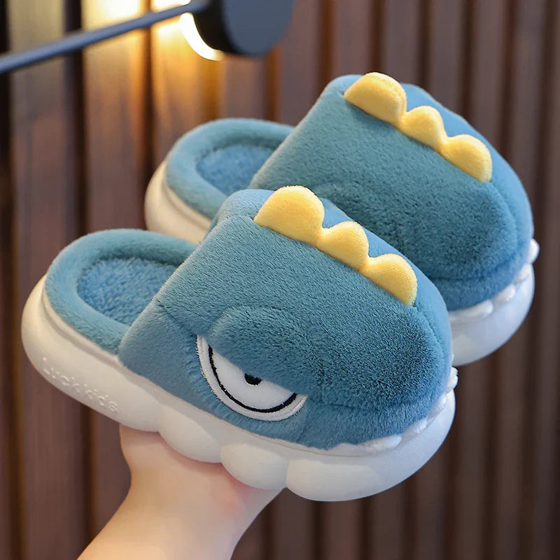 Light blue dinosaur-themed slippers held by a hand against a blurred background