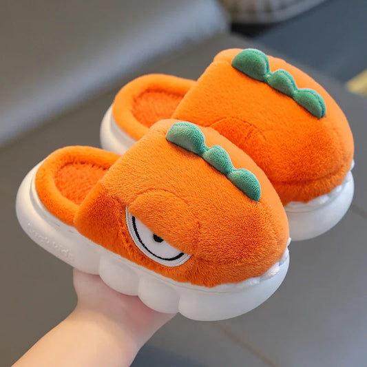 Pair of orange plush slippers with a face design held by a hand on a neutral background