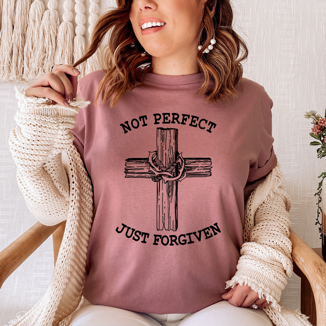 Person wearing a pink sweatshirt with a cross design and text, sitting on a wooden chair.