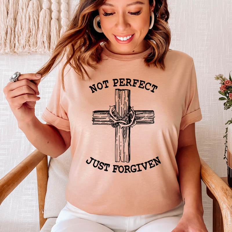 Woman wearing a beige t-shirt with a cross and chain design and text 'Not Perfect Just Forgiven'.