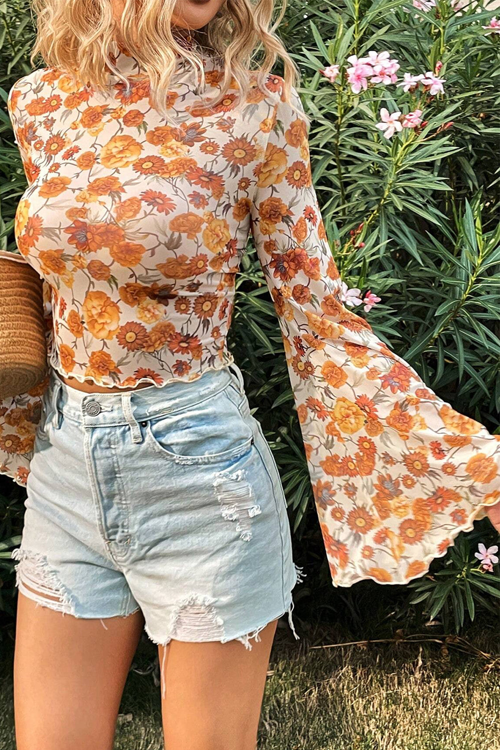 Person wearing a floral blouse and denim shorts standing in front of green foliage.