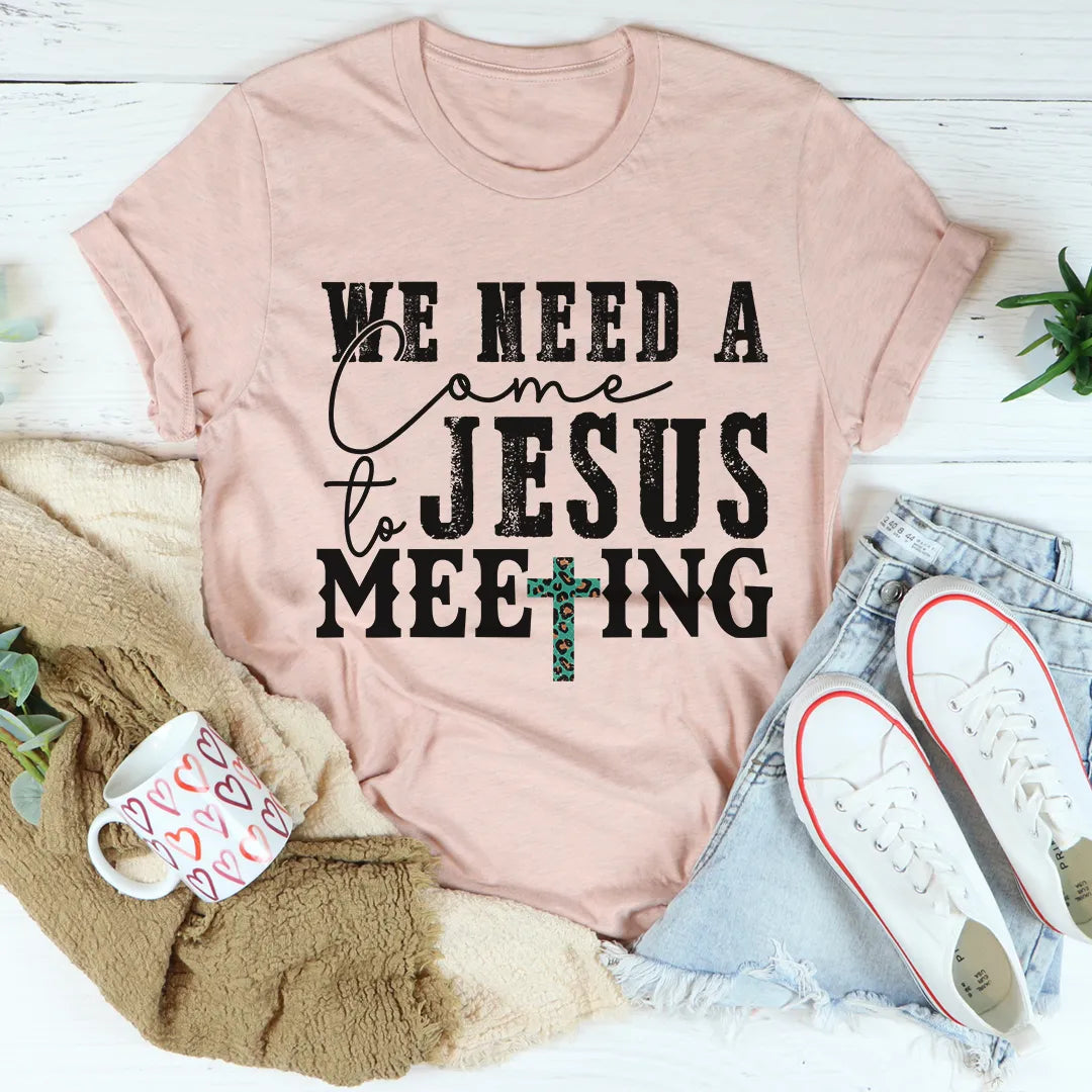 Pink t-shirt with 'We Need a Jesus Meeting' text on a white surface with casual items.