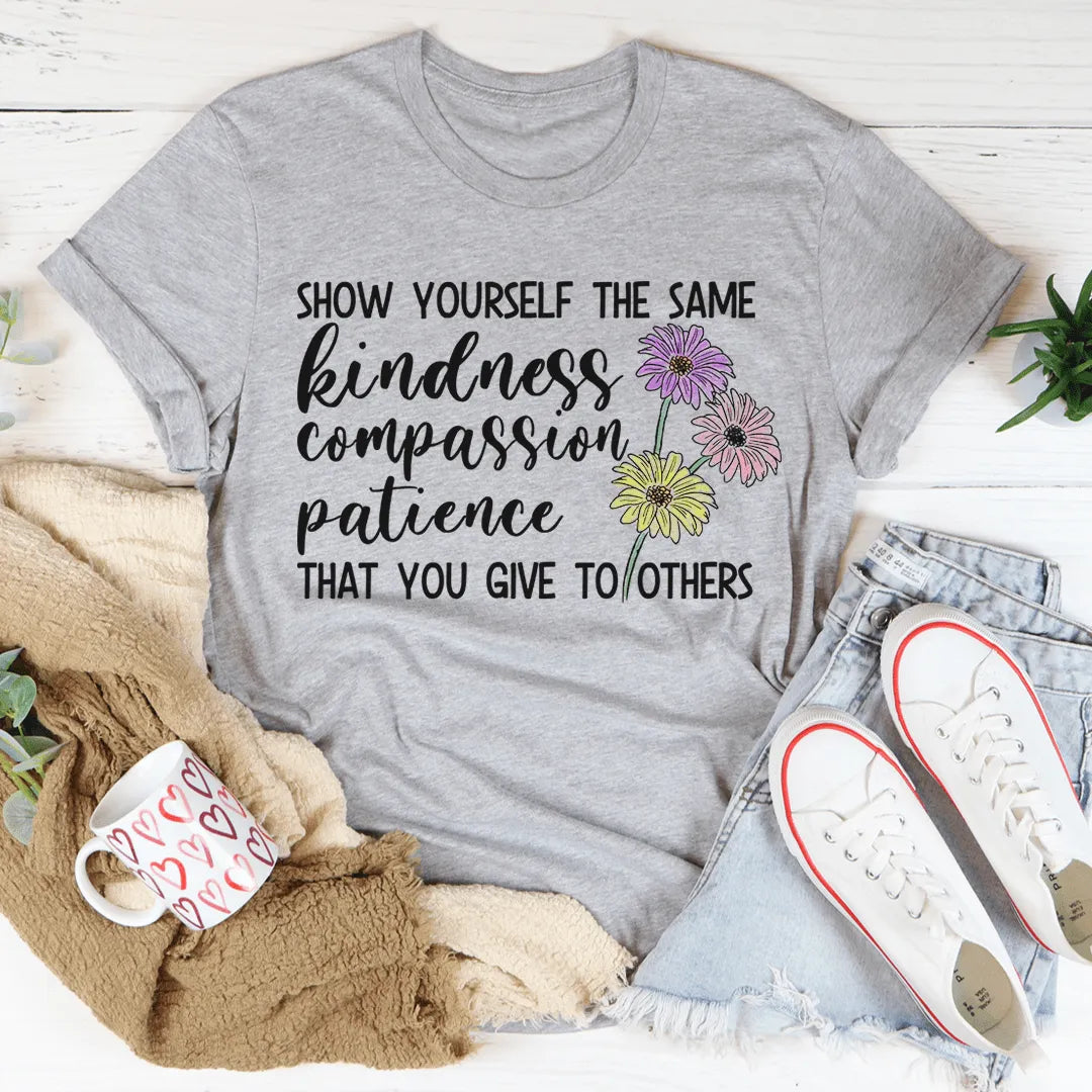 Gray t-shirt with motivational quote and flowers, placed on a wooden surface with accessories.
