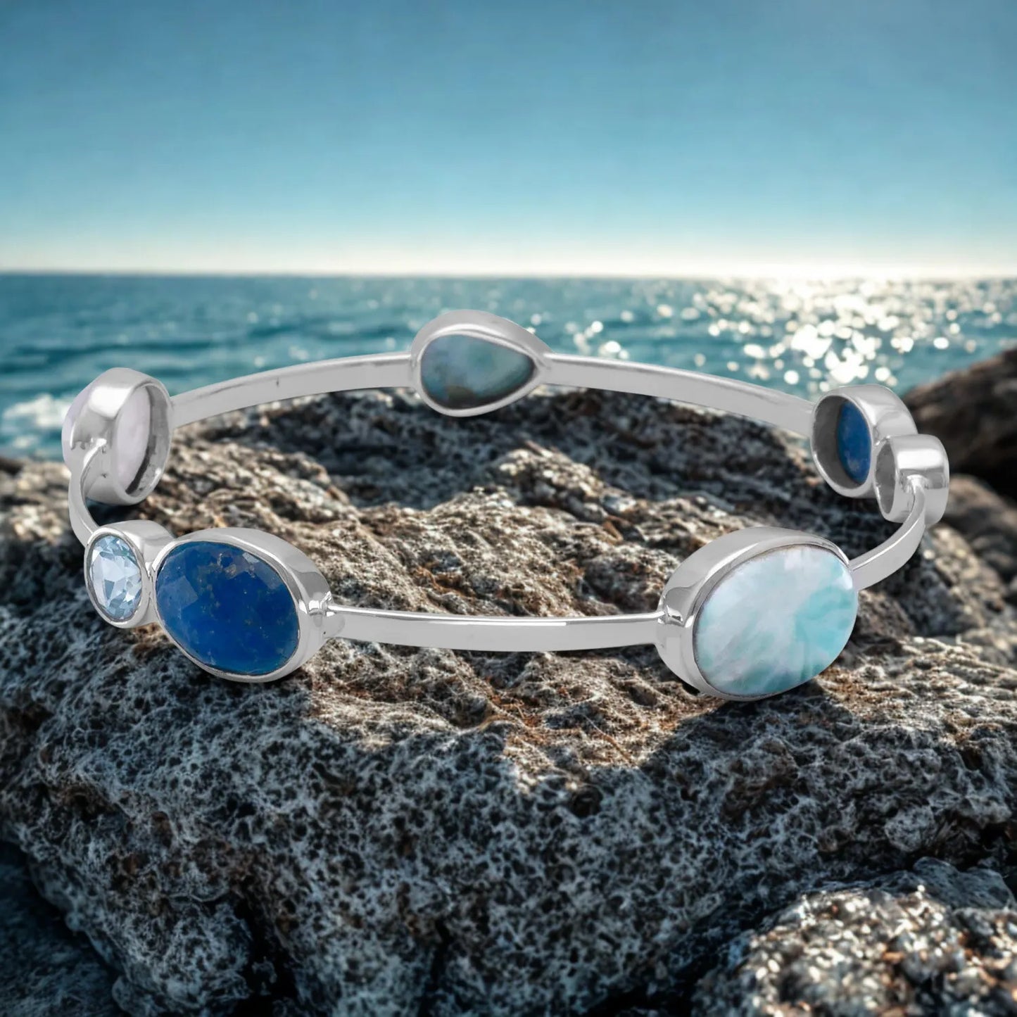 Silver bracelet with blue and green stones on a rock by the ocean