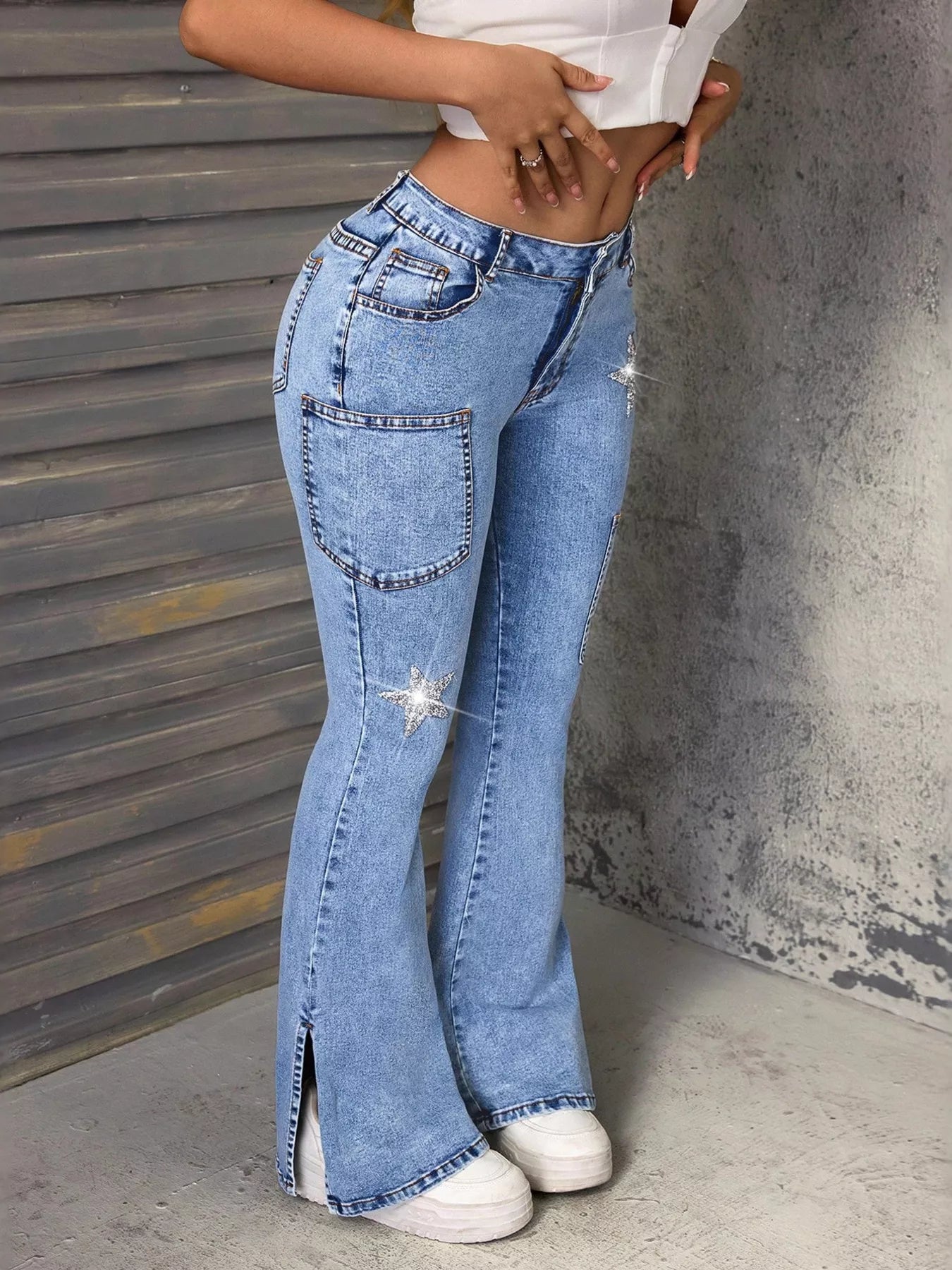 Lady wearing slit star flare leg blue denim jeans paired with a white tank top and white tennis shoes, with additional shoes visible in the background.