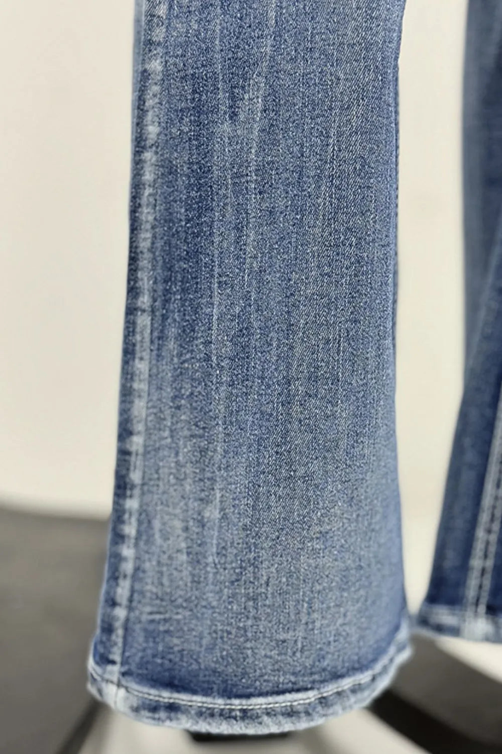Woman wearing long boot cut acid wash blue jeans with star embroidered pockets, styled with sandals, with dried grass visible in the background.