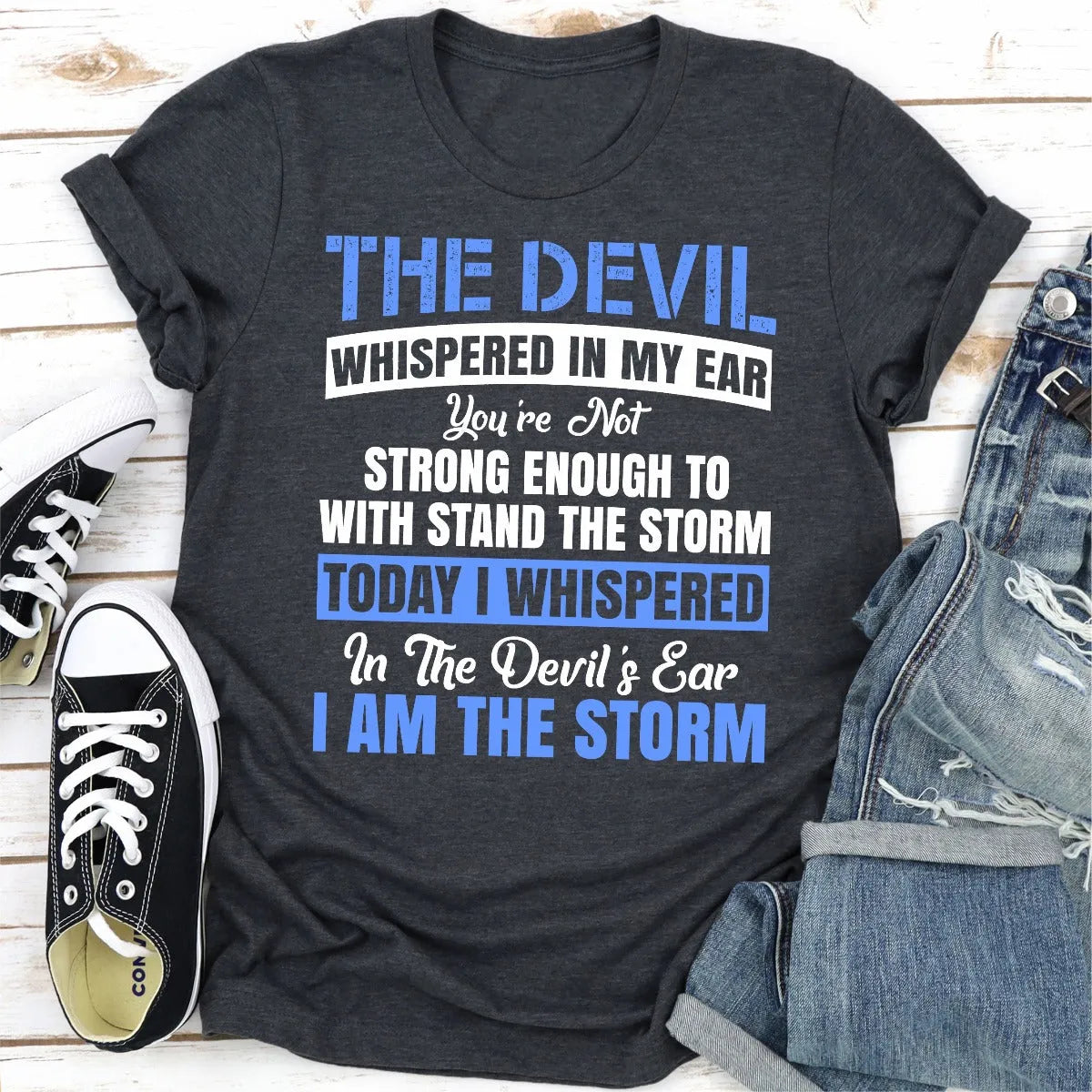 Black t-shirt with motivational quote on a wooden surface with sneakers and jeans.