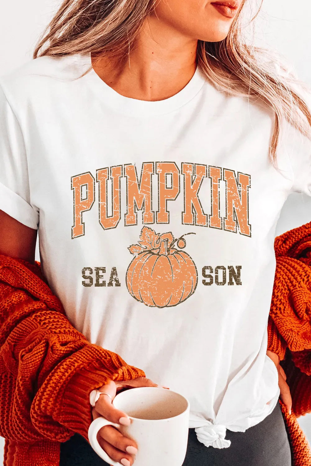 Person wearing a white t-shirt with 'Pumpkin Season' print, holding a mug.