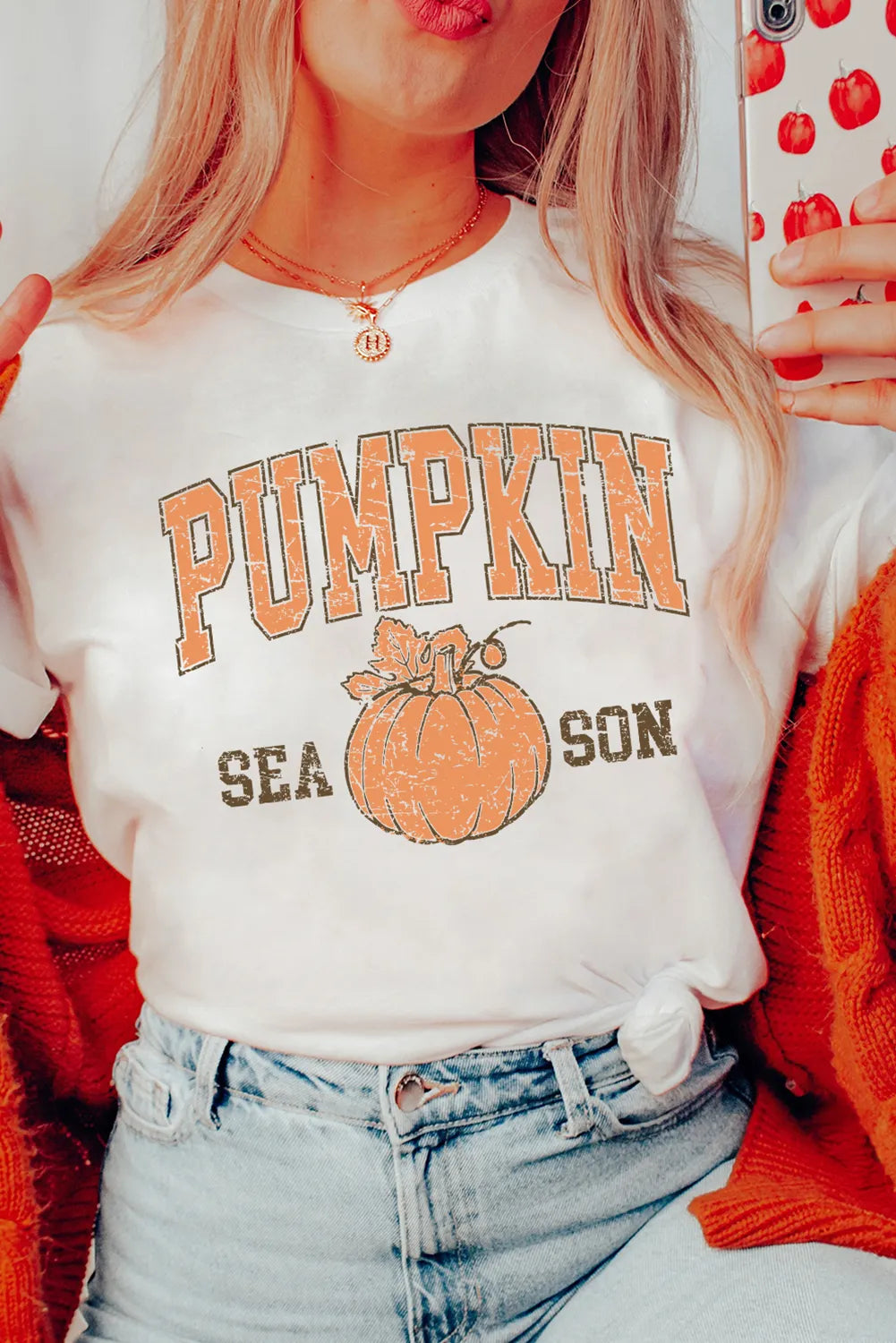 Person wearing a white t-shirt with 'Pumpkin Season' print, holding a phone with a red case.