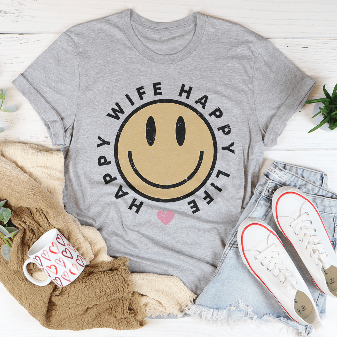 Gray t-shirt with smiley face design and text, surrounded by casual items on a light wooden surface.